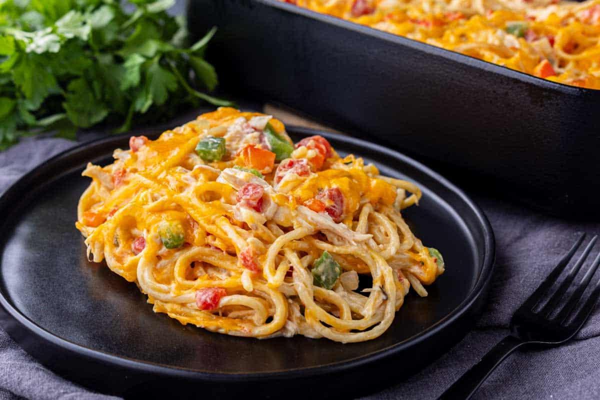 33 einfache und günstige Gerichte (die Ihre Familie auch wirklich essen möchte) 2 Ein Teller mit gebackenem Spaghetti-Auflauf mit Käse, Paprika und Tomaten, mit einer Auflaufform und frischer Petersilie im Hintergrund.
