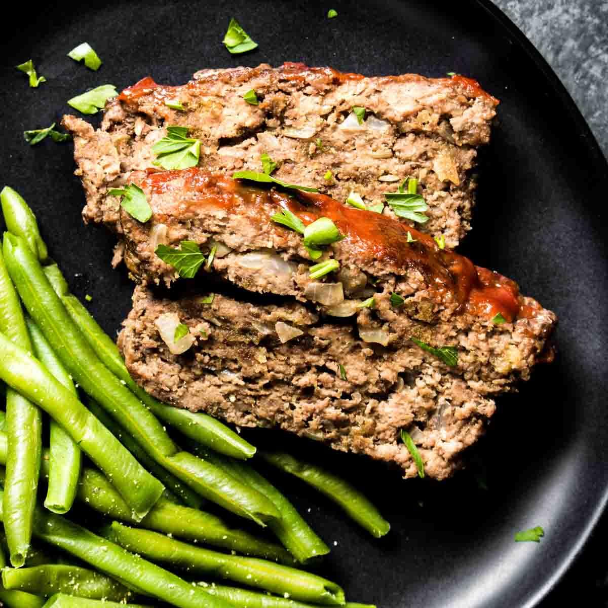 Keto Hackbraten – Low-Carb-Soulfood 2 Ketogener Hackbraten und grüne Bohnen auf einem schwarzen Teller angerichtet.