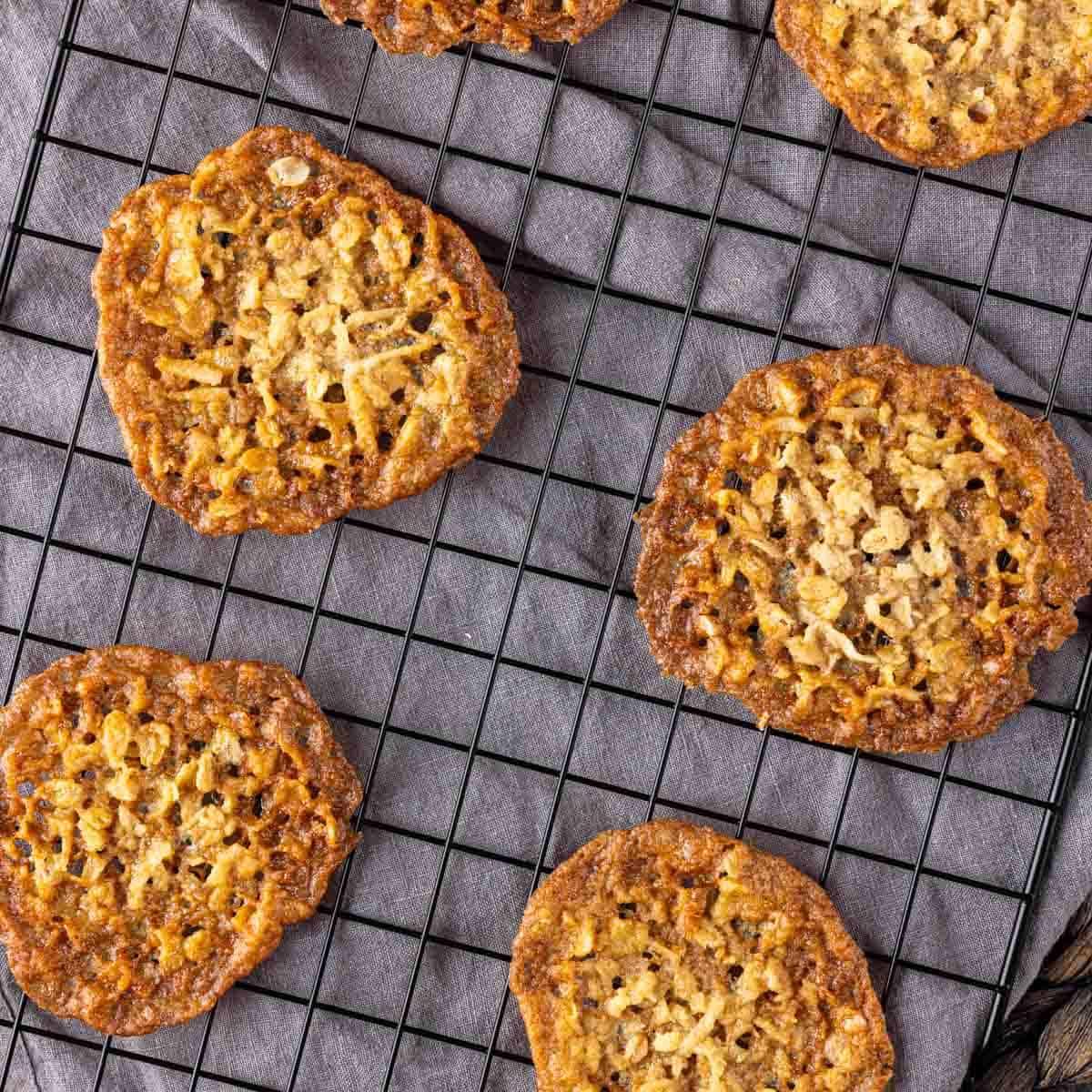 Knusprige Kokos-Haferflocken-Spitzenplätzchen 2 Knusprige Kokos-Kekse auf einem Abkühlgitter.
