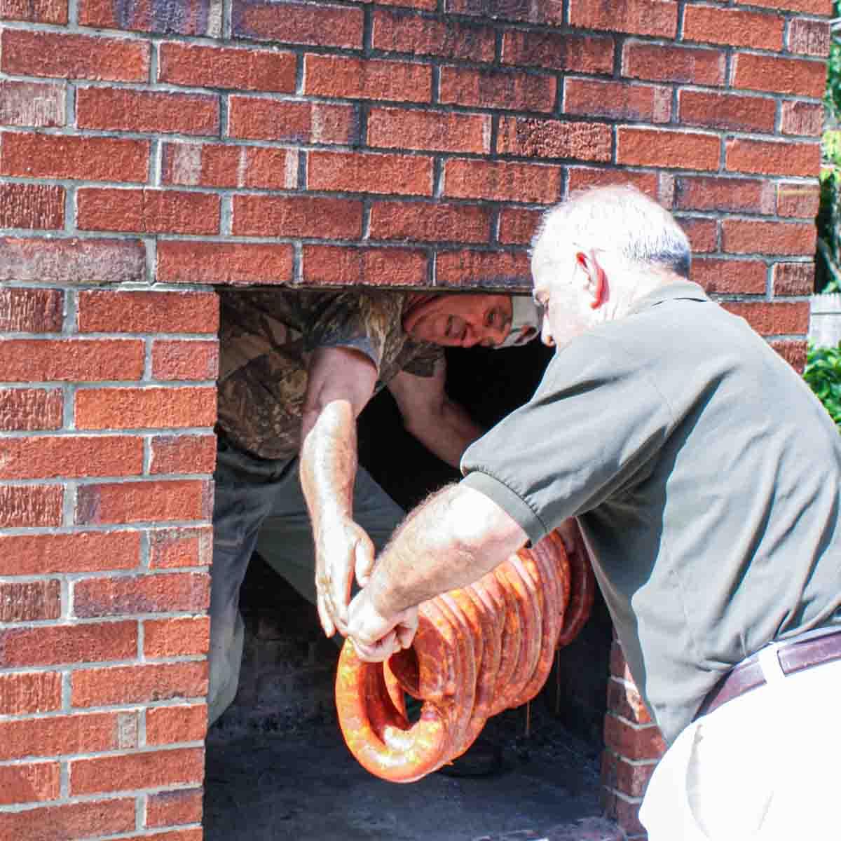 Hausgemachtes Chouriço herstellen: Eine traditionelle portugiesische Wurst 11 Zwei Männer, die portugiesische Wurst in einen gemauerten Kamin legen.