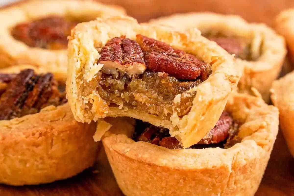 Unwiderstehliche Desserts mit Pekannusskuchenfüllung 11 Nahaufnahme von Mini-Pekannusskuchen mit knusprigen Böden und Pekannuss-Topping, ein Kuchen zeigt die innere Füllung.