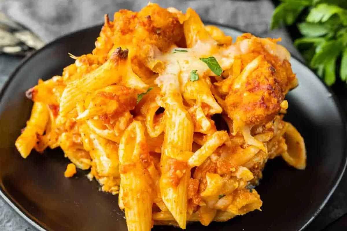 **Schnelle und einfache Hähnchengerichte für vielbeschäftigte Familien** 12 Eine Portion gebackener Ziti mit geschmolzenem Käse und Tomatensauce auf einem schwarzen Teller, garniert mit Basilikum.