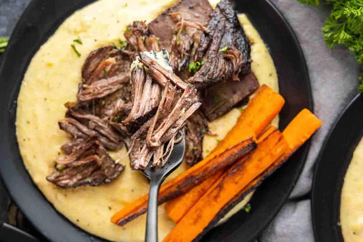**Ein Galentine’s-Schmaus für deine Mädels** 12 Teller mit geschmortem Rindfleisch, cremiger Polenta und gerösteten Karottensticks, garniert mit Kräutern.