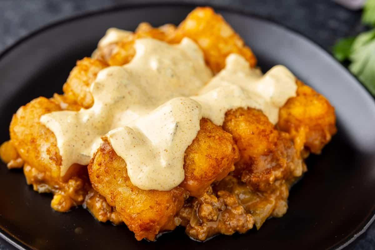 33 einfache und günstige Gerichte (die Ihre Familie auch wirklich essen möchte) 13 Ein Teller mit Tater Tot Auflauf, überzogen mit cremiger Soße, der goldbraune Tater Tots und eine Hackfleischmischung darunter zeigt.