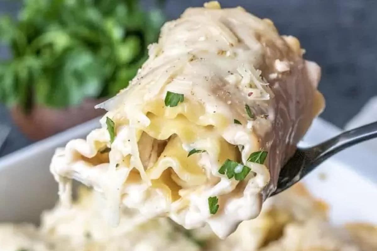 **Schnelle und einfache Hähnchengerichte für vielbeschäftigte Familien** 13 Eine Gabel hebt eine Portion cremiger, geschichteter Lasagne, garniert mit Kräutern, mit einer Beilage frischem Grün im Hintergrund.