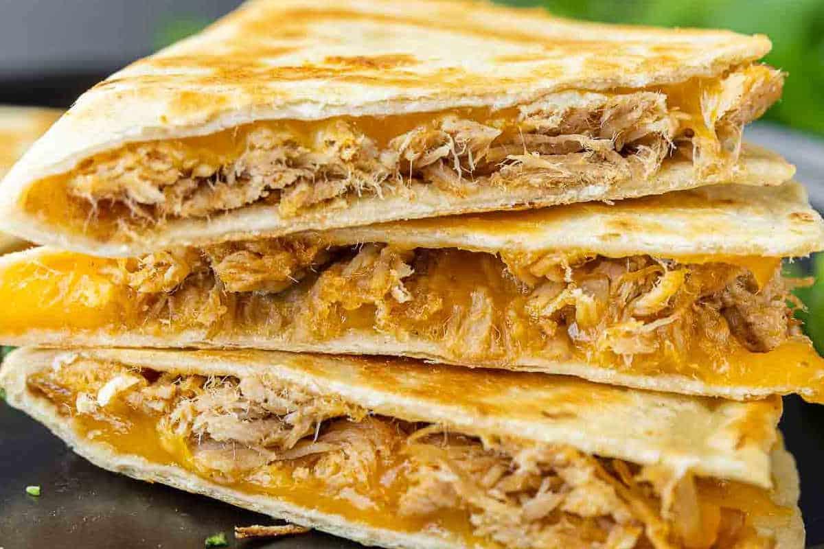 Festliche Abendessenrezepte für den Cinco de Mayo 13 Nahaufnahme von Pulled Pork Quesadillas, goldbraun gebacken, mit geschmolzenem Käse, serviert auf einem rustikalen Untergrund.