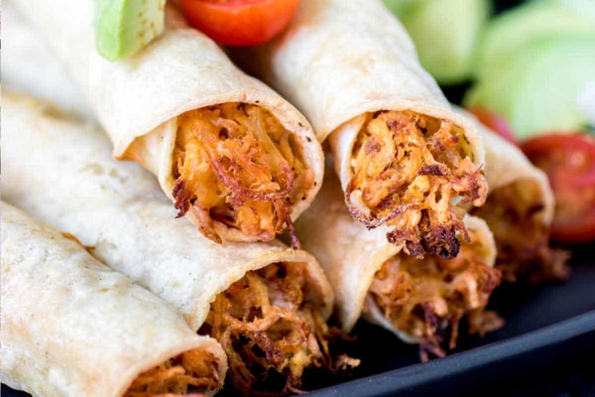 Festliche Abendessenrezepte für den Cinco de Mayo 14 Nahaufnahme von Hähnchen-Taquitos auf einem Teller, garniert mit geschnittenen Gurken und Kirschtomaten.