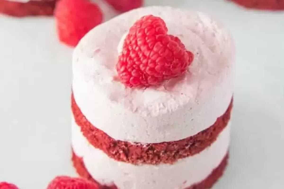 **Ein Galentine’s-Schmaus für deine Mädels** 16 Kleiner geschichteter Red Velvet Kuchen mit weißer Glasur, belegt mit einer Himbeere, auf einer weißen Oberfläche.