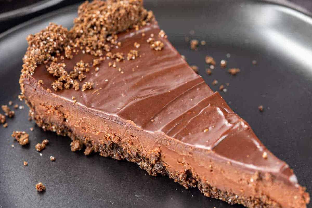 **Ein Galentine’s-Schmaus für deine Mädels** 17 Ein Stück Schokoladen-Käsekuchen mit bröseligem Boden auf einem dunklen Teller.
