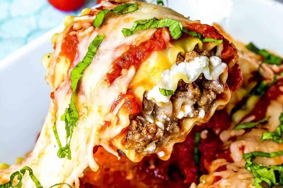 33 einfache und günstige Gerichte (die Ihre Familie auch wirklich essen möchte) 18 Nahaufnahme einer käsigen Lasagne-Roulade, gefüllt mit Hackfleisch und Ricotta-Käse, belegt mit Tomatensauce und frischem Basilikum.