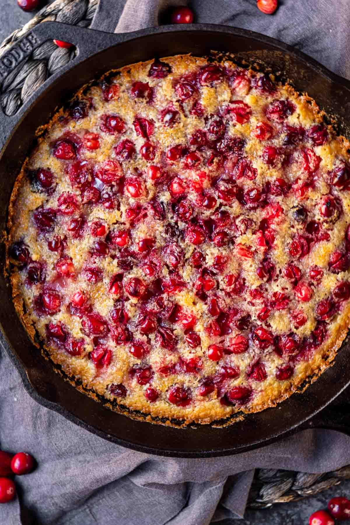 Cranberry-Streuselkuchen 3 Ein Preiselbeer-bedecktes Dessert in einer Gusseisenpfanne, auf einem dunklen Tuch platziert.