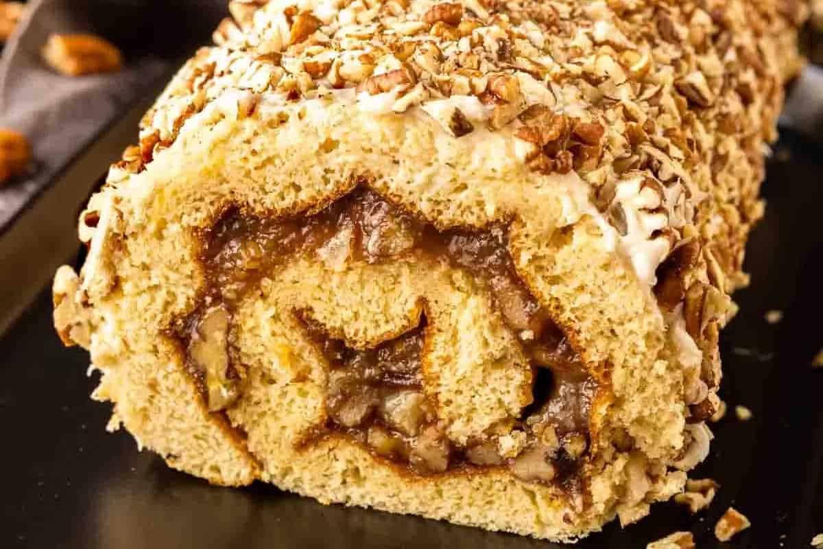 Unwiderstehliche Desserts mit Pekannusskuchenfüllung 3 Nahaufnahme einer geschnittenen Biskuitrolle, belegt mit gehackten Nüssen und gefüllt mit einer zimtgewürzten Mischung, präsentiert auf einer schwarzen Oberfläche.