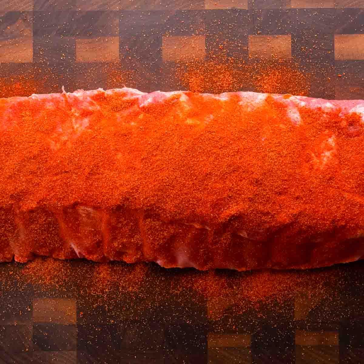 St. Louis Style Spareribs: Langsam gegarte Perfektion 3 Ein rohes St. Louis-Style Rippchen, großzügig mit rotem Gewürz-Rub bedeckt, auf einem Holzschneidebrett.