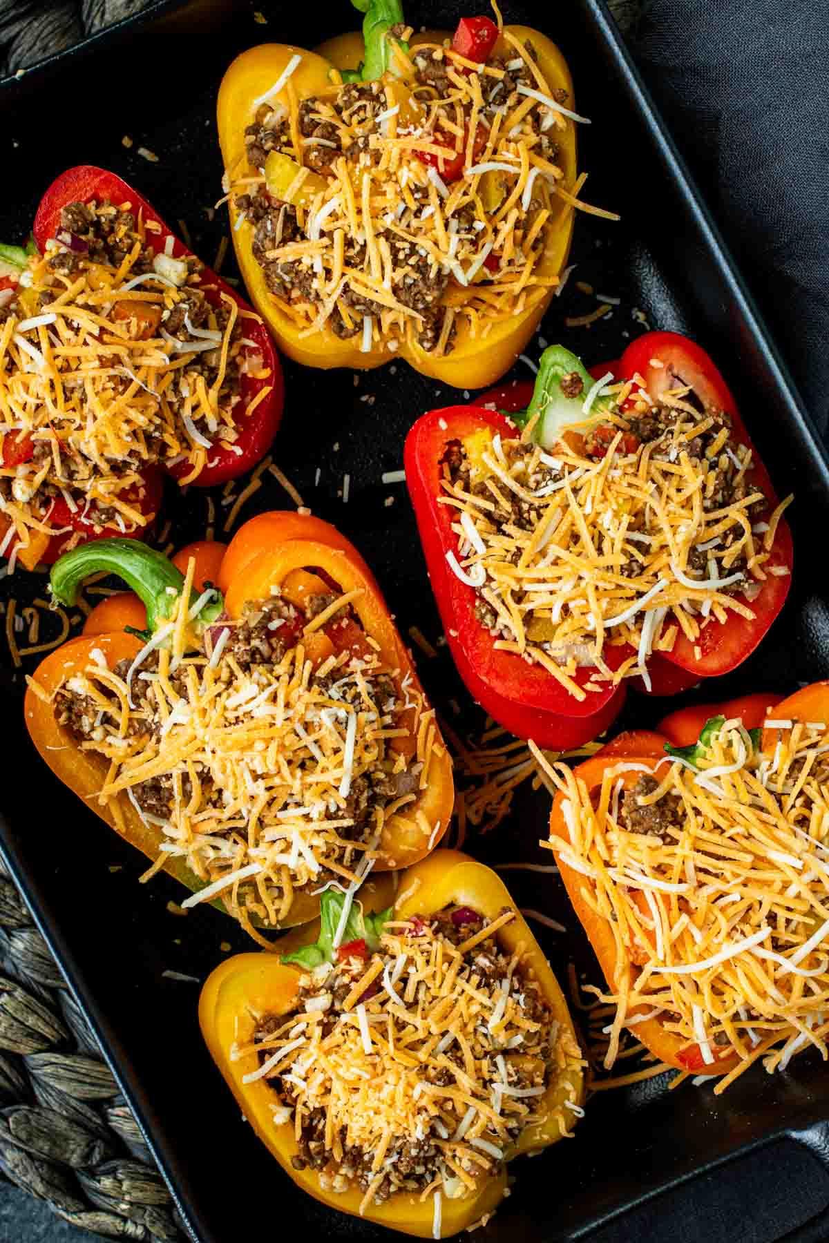 Leichte Mexikanische Gefüllte Paprika mit Reis 8 Bunte Paprikahälften in einer Auflaufform, gefüllt mit Hackfleisch und Reis, mit Käse bestreut, bereit zum Backen.