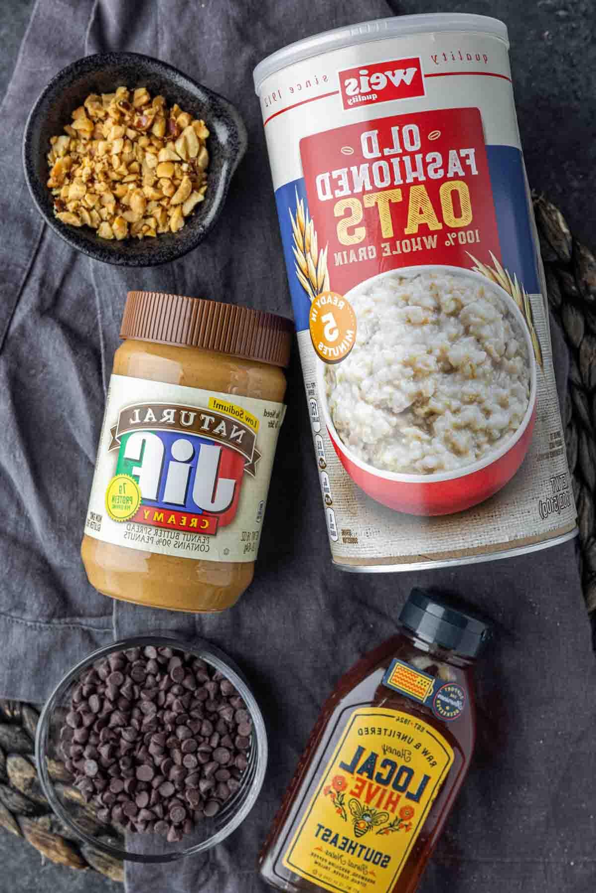 Erdnussbutter-Energiekugeln 3 Zutaten für Erdnussbutter-Energiebällchen: Erdnussbutter, Haferflocken, Honig, Schokoladenstückchen, Erdnüsse auf einer Arbeitsfläche