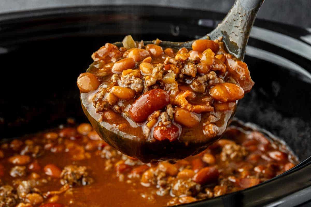 33 einfache und günstige Gerichte (die Ihre Familie auch wirklich essen möchte) 26 Eine Kelle hebt eine Portion Chili mit Bohnen und Hackfleisch aus einem schwarzen Slow Cooker.