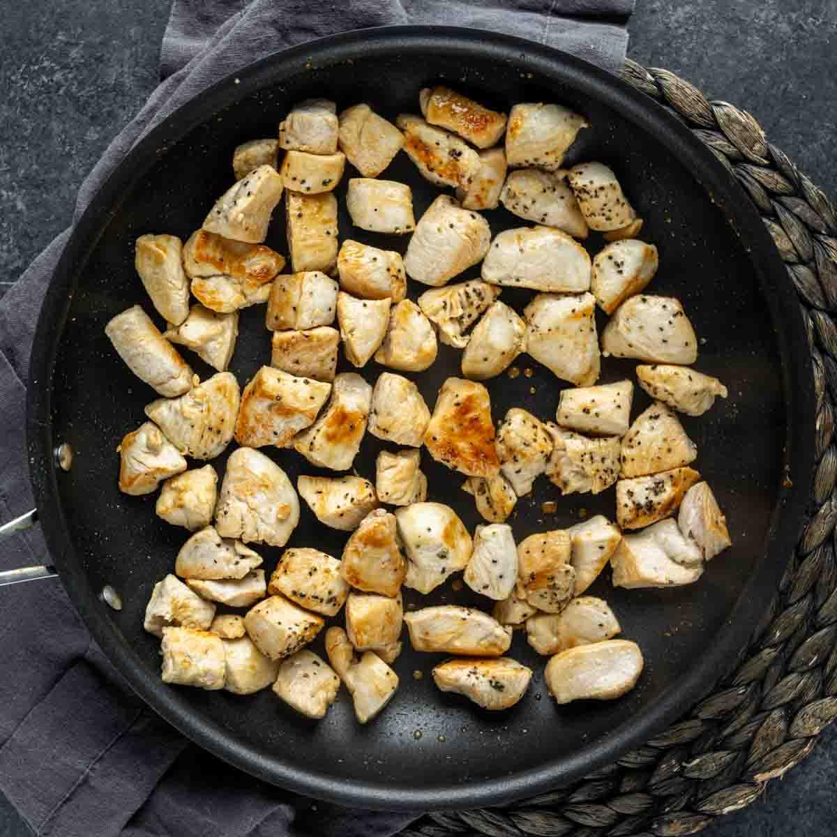 Cremige Florentiner Hähnchen-Pasta 4 Gewürfelte Hähnchenbruststücke werden in einer Bratpfanne für Hähnchen Florentiner Auflauf gekocht.