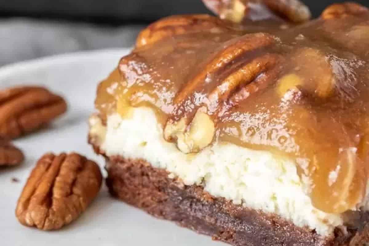Unwiderstehliche Desserts mit Pekannusskuchenfüllung 4 Nahaufnahme eines Pekannusskuchen-Käsekuchen-Riegels mit einer Schicht karamellisierter Pekannuss-Topping und einem cremigen Käsekuchenkern auf einem weißen Teller.