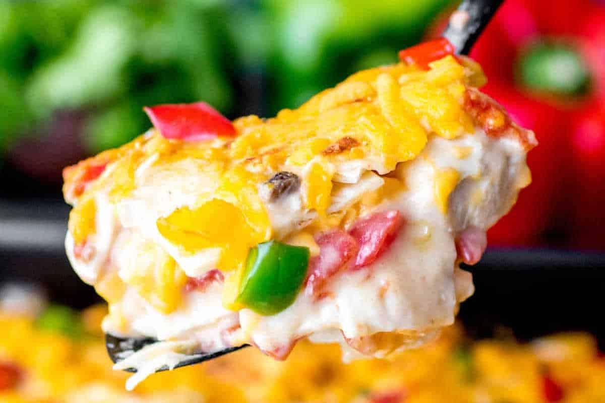 33 einfache und günstige Gerichte (die Ihre Familie auch wirklich essen möchte) 5 Nahaufnahme eines Tellers mit käsiger Lasagne mit sichtbaren Stücken roter und grüner Paprika, mit einem Spatel angehoben.