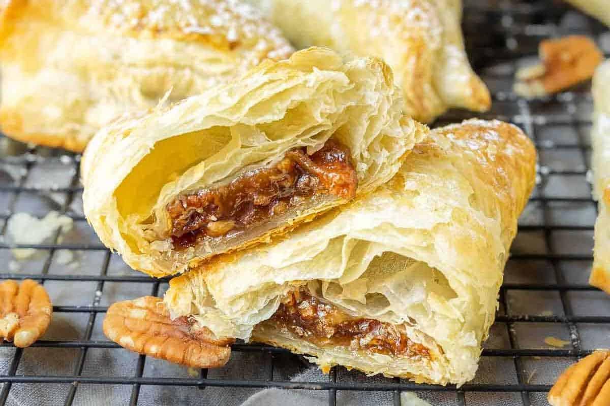 Unwiderstehliche Desserts mit Pekannusskuchenfüllung 5 Ein Blätterteiggebäck ist in zwei Hälften geschnitten und enthüllt eine Füllung aus Pekannüssen und Karamell. Es liegt auf einem Kühlgitter neben verstreuten Pekannusshälften.