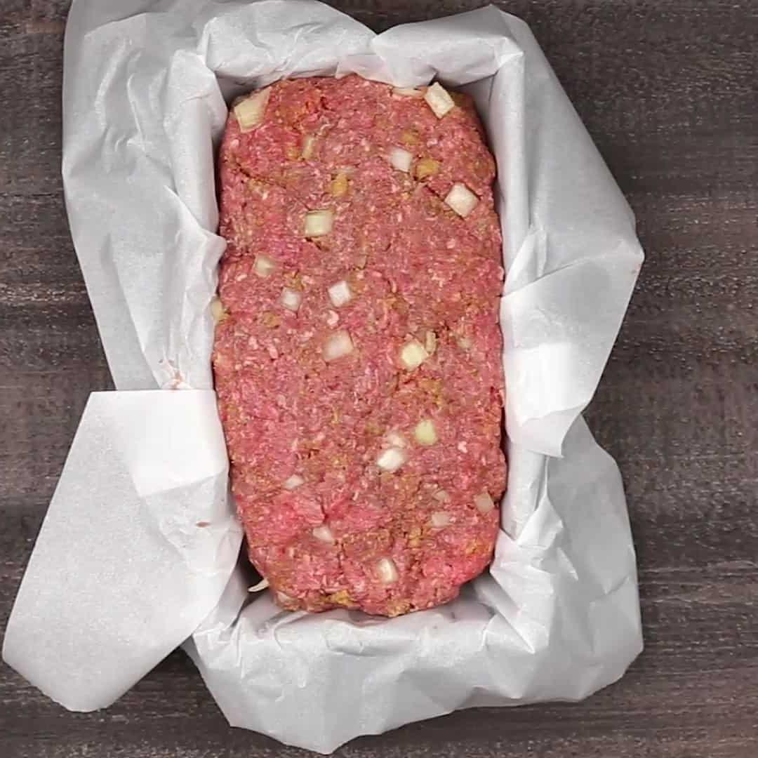 Keto Hackbraten – Low-Carb-Soulfood 5 Ketogener Hackbraten fest in einer mit Backpapier ausgelegten Kastenform auf einem rustikalen Holztisch präsentiert.