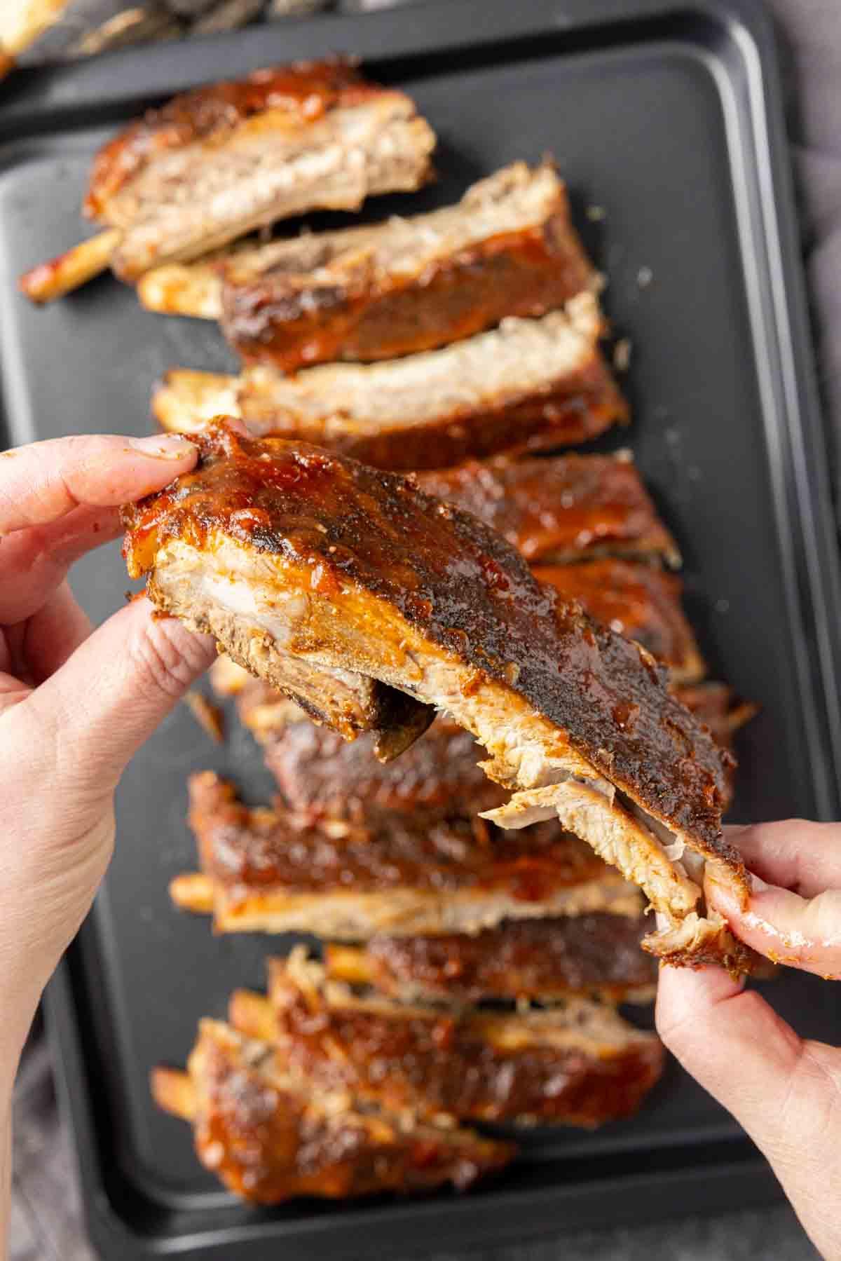 St. Louis Style Spareribs: Langsam gegarte Perfektion 5 Die Hand einer Person zieht ein zartes, gekochtes St. Louis-Style Rippchen von einem Tablett voller Barbecue-Rippchen.