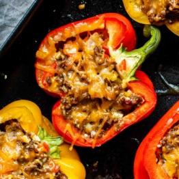 Leichte Mexikanische Gefüllte Paprika mit Reis 10 Gefüllte Paprika mit Hackfleisch, gewürfelten Tomaten und geschmolzenem Käse, auf einem dunklen Teller serviert.