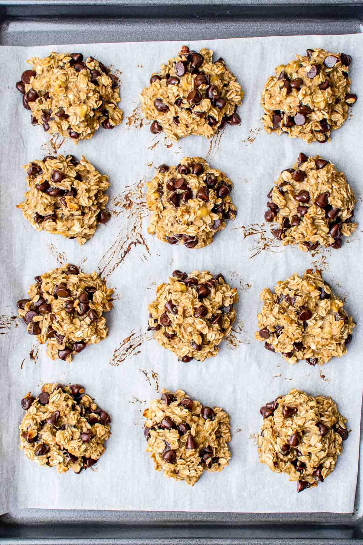 Gesunde Haferflockenkekse – Einfaches Frühstück oder Snack! 6 Ein Backblech mit zwölf Schokostückchen-Haferflockenkeksen auf Backpapier, bereit zum Backen.