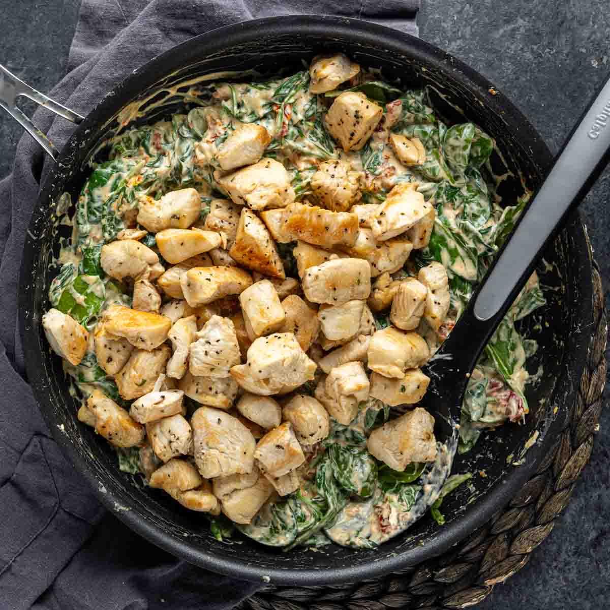 Cremige Florentiner Hähnchen-Pasta 7 Gekochte gewürfelte Hähnchenbrust in einer cremigen Hähnchen Florentiner Auflaufsauce in einer schwarzen Pfanne.