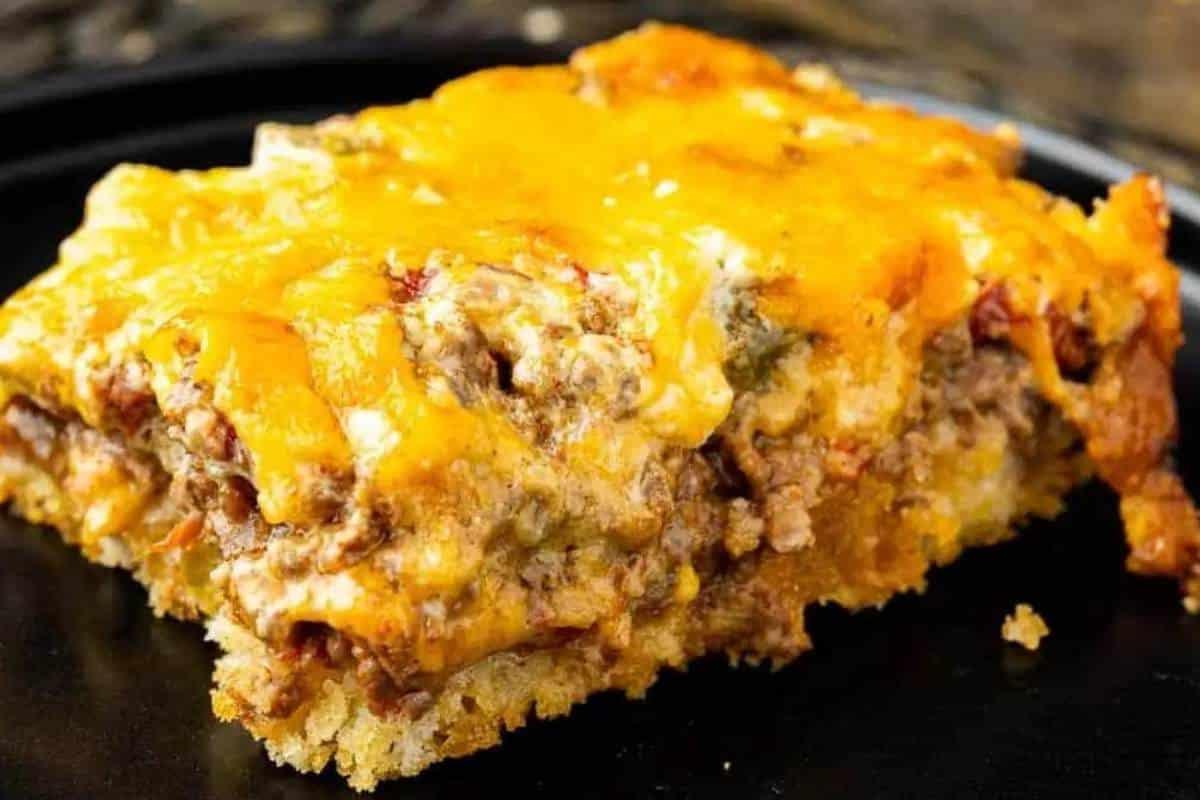 33 einfache und günstige Gerichte (die Ihre Familie auch wirklich essen möchte) 7 Nahaufnahme eines Stücks John Wayne Auflauf mit geschmolzenem Käse, das Schichten von Hackfleisch, Gemüse und einer Biskuitbasis zeigt.