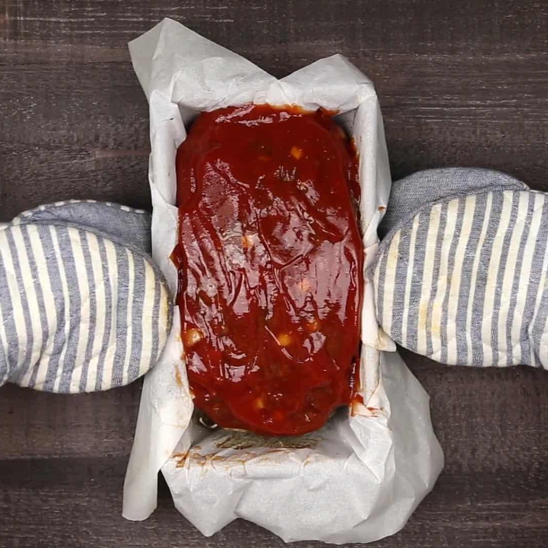 Keto Hackbraten – Low-Carb-Soulfood 7 Der teilweise gebackene ketogene Hackbraten in der Kastenform, von zwei Händen für den nächsten Schritt gehalten.