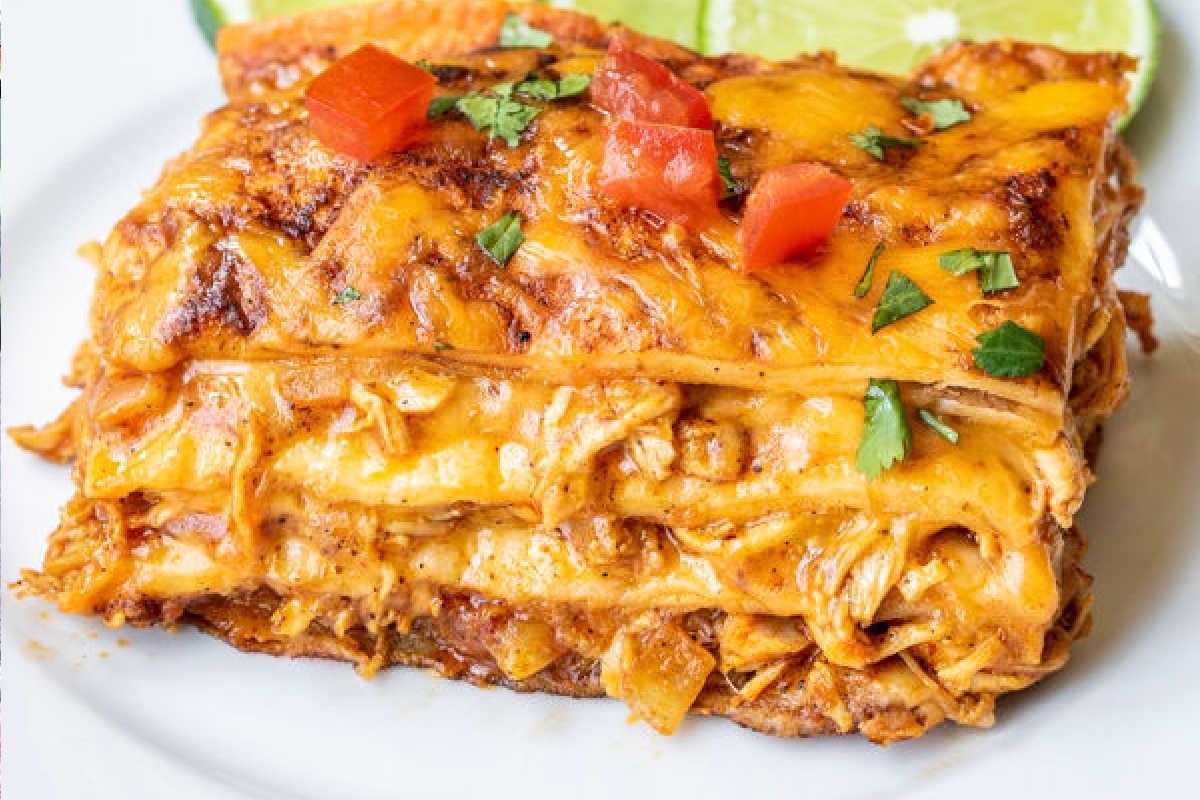 **Schnelle und einfache Hähnchengerichte für vielbeschäftigte Familien** 7 Nahaufnahme eines Stücks käsigen Enchilada-Auflaufs, garniert mit Koriander und gewürfelten Tomaten, serviert auf einem weißen Teller.