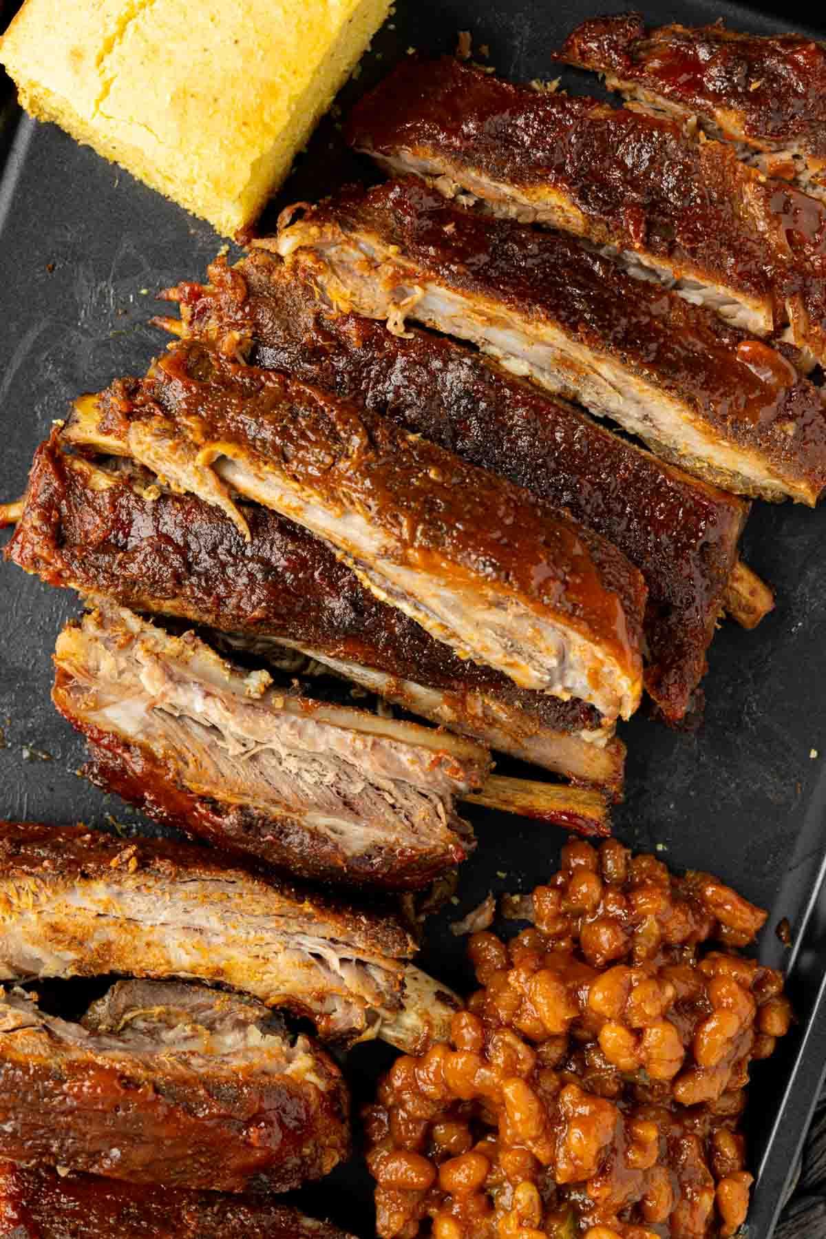 St. Louis Style Spareribs: Langsam gegarte Perfektion 7 Geschnittene St. Louis-Style Ribs serviert mit Maisbrot und gebackenen Bohnen auf einem schwarzen Teller.