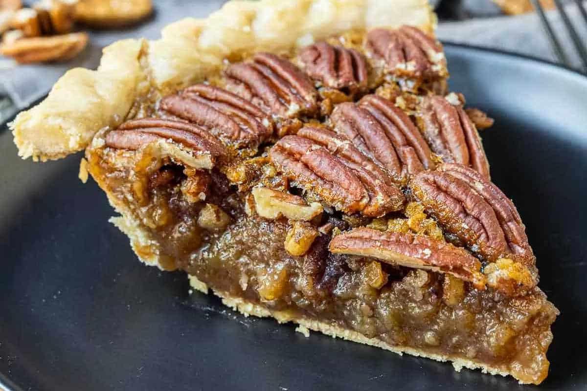 Unwiderstehliche Desserts mit Pekannusskuchenfüllung 8 Eine Scheibe Pekannusskuchen auf einem dunklen Teller, mit knusprigem Boden, klebriger Füllung und ganzen Pekannüssen belegt.
