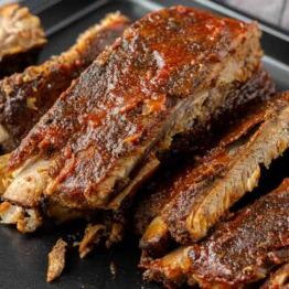 St. Louis Style Spareribs: Langsam gegarte Perfektion 8 Saftige St. Louis-Style Ribs auf einem schwarzen Teller serviert, mit einer reichhaltigen, knusprigen Kruste und zartem Fleisch, das vom Knochen fällt.