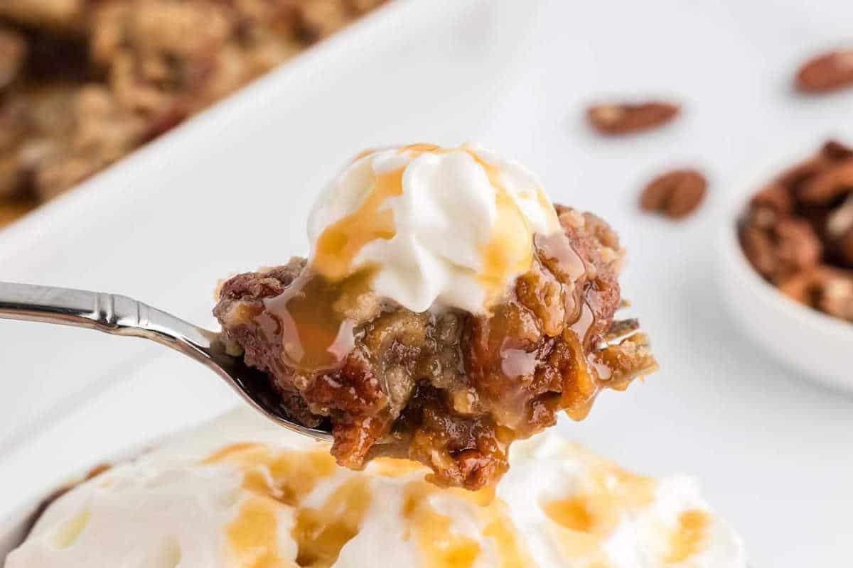 Unwiderstehliche Desserts mit Pekannusskuchenfüllung 9 Nahaufnahme eines Löffels Brotpudding, belegt mit Schlagsahne und Karamell-Drizzle, über einem Teller gehalten. Pekannüsse sind im Hintergrund.
