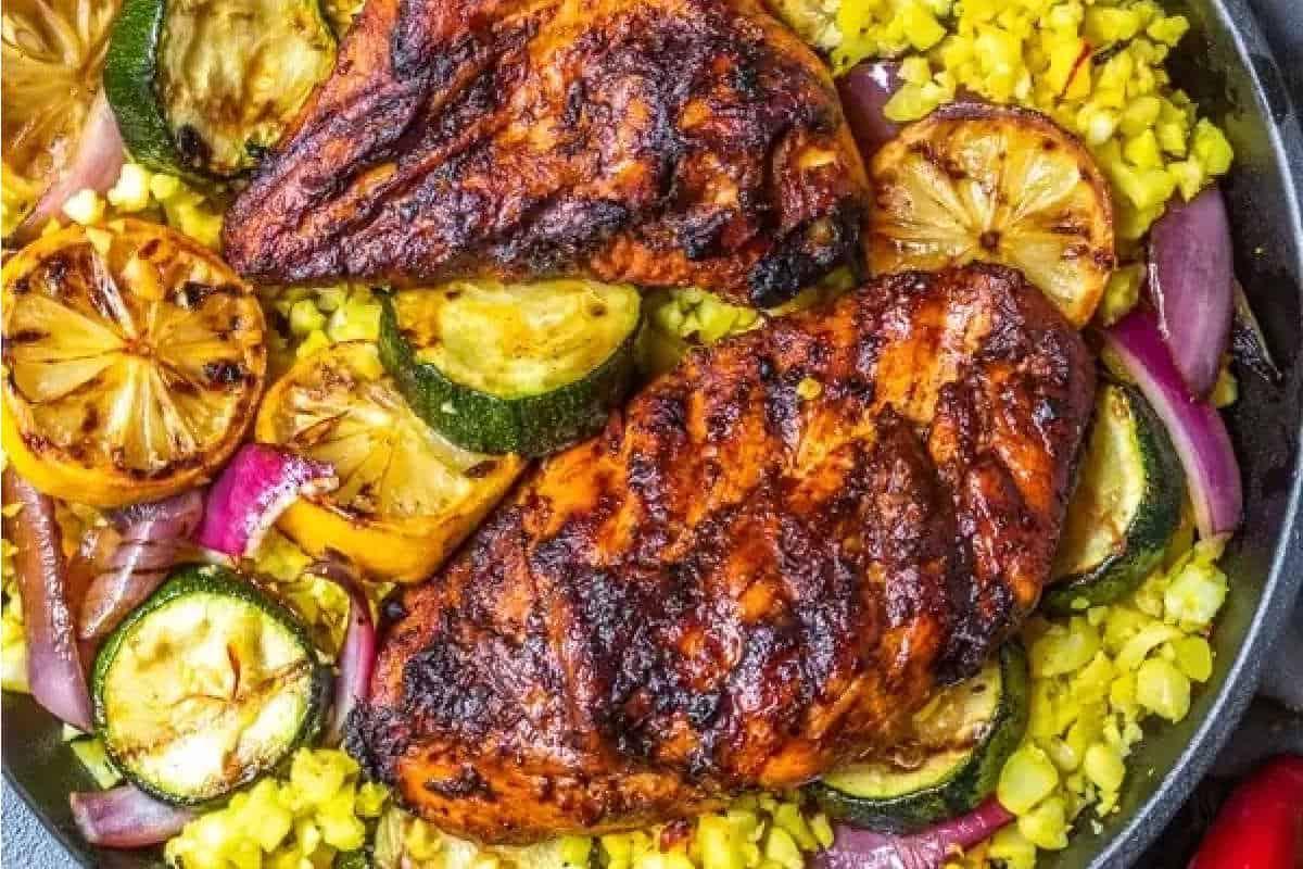 **Schnelle und einfache Hähnchengerichte für vielbeschäftigte Familien** 9 Gegrillte Hähnchenbrüste mit verkohlten Zitronenscheiben, Zucchini und roten Zwiebeln, serviert über gelbem Reis in einer Pfanne.