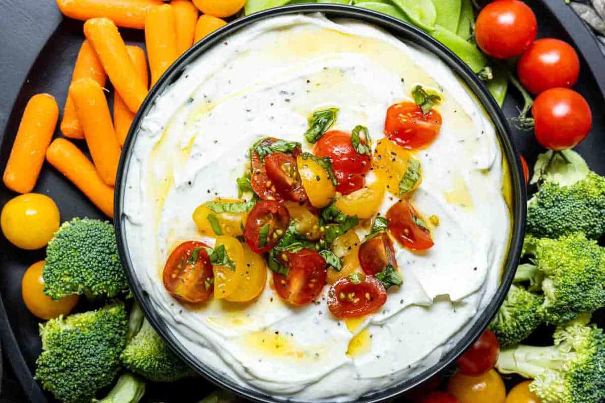**Ein Galentine’s-Schmaus für deine Mädels** 9 Eine Schüssel cremiger Dip, belegt mit gehackten Tomaten und Kräutern, umgeben von Brokkoli, Kirschtomaten, Zuckererbsen und Babykarotten.