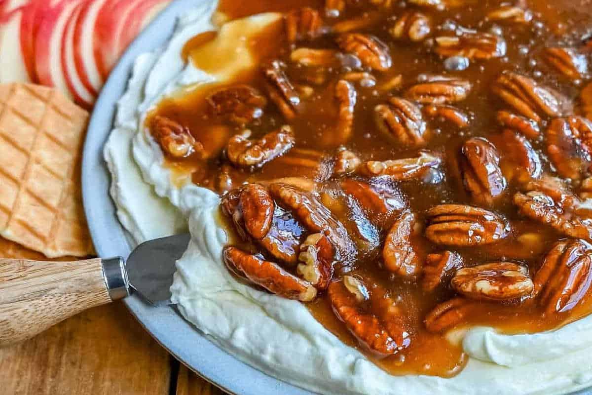 Unwiderstehliche Desserts mit Pekannusskuchenfüllung 10 Nahaufnahme eines Desserts, belegt mit karamellisierten Pekannüssen, Sahne, und umgeben von Apfelscheiben und Waffelstücken auf einem Teller.