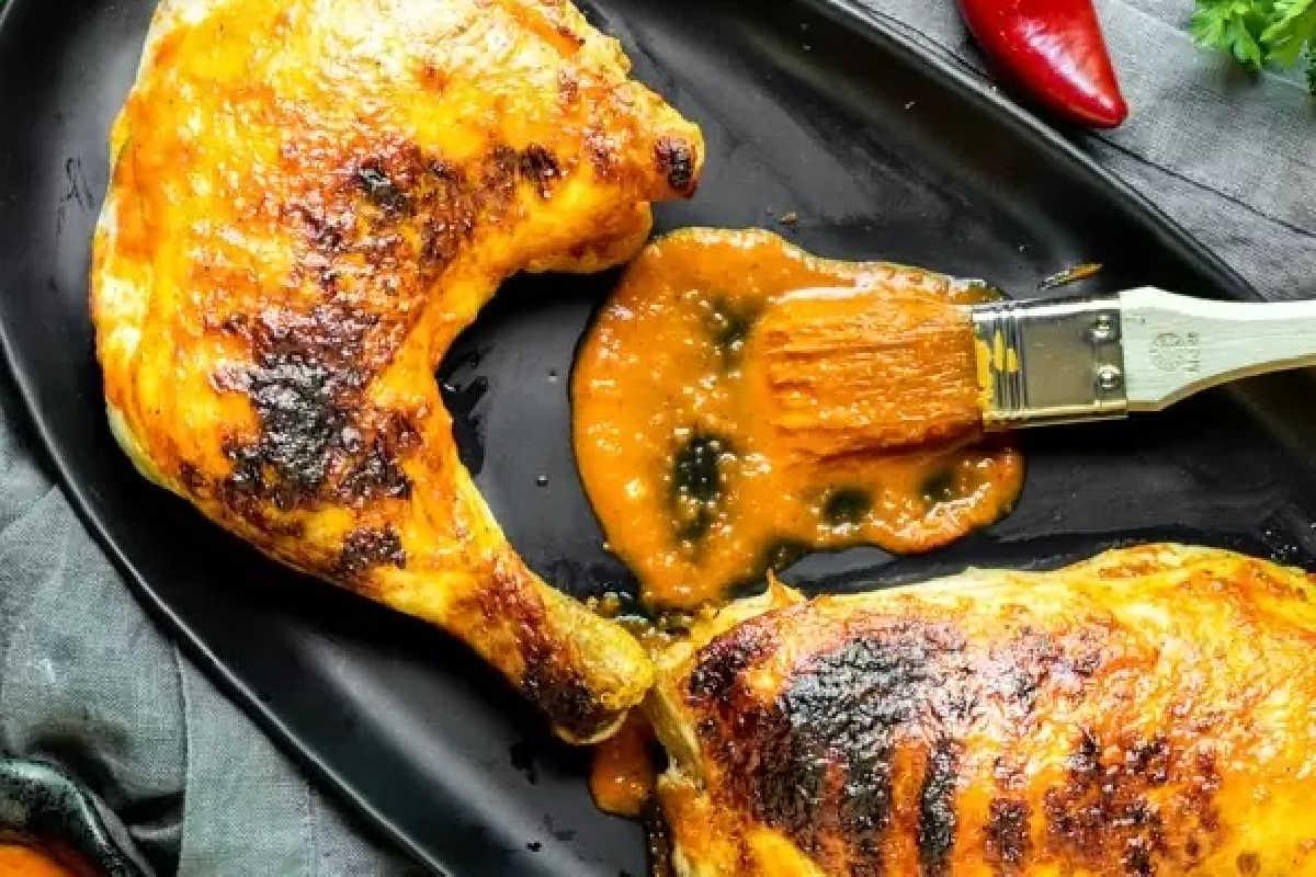 **Schnelle und einfache Hähnchengerichte für vielbeschäftigte Familien** 10 Gegrillte Hähnchenschenkel auf einer schwarzen Pfanne mit einem Pinsel, der Sauce aufträgt, garniert mit Kräutern und einer Chilischote.