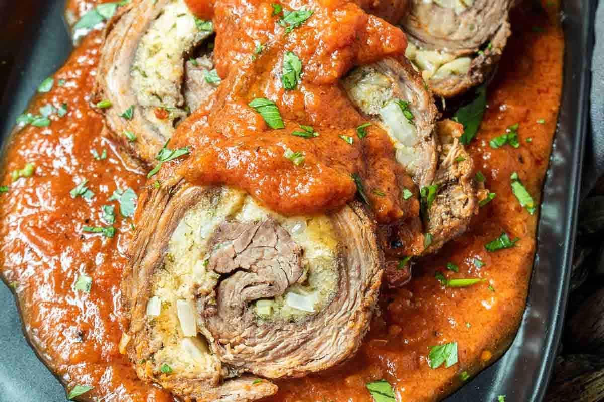 **Ein Galentine’s-Schmaus für deine Mädels** 10 Scheiben von Rinderroulade, belegt mit Tomatensauce und garniert mit gehackten Kräutern auf einem schwarzen Teller.