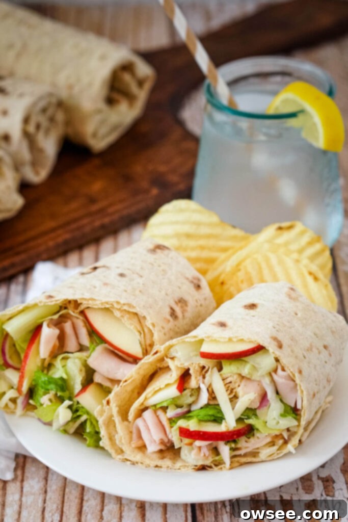 Crisp Turkey Apple Swiss Wraps 2 A Turkey Swiss and Apple Wrap cut in half and served with potato chips on a white plate.
