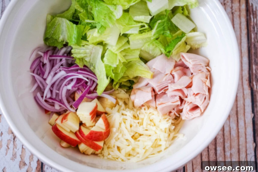 Crisp Turkey Apple Swiss Wraps 9 A white bowl of chopped lettuce, turkey, and apples with shredded swiss cheese and red onion.