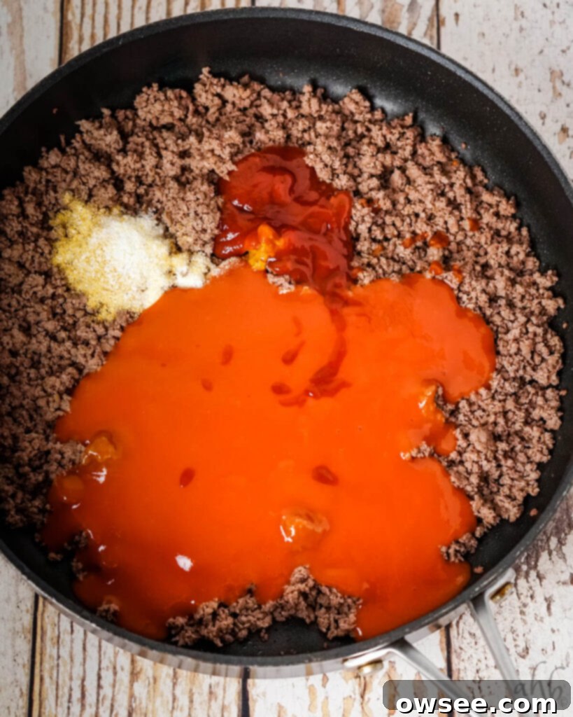 Sloppy Joe Stuffed Garlic Bread 6 Tomato soup, Worcestershire sauce, yellow mustard, ketchup, onion powder, salt, garlic powder, and browned ground beef in a medium black skillet, ready for simmering.