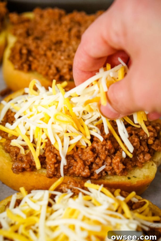 Sloppy Joe Stuffed Garlic Bread 8 Shredded Colby Jack cheese being sprinkled over the garlic bread and sloppy joe meat mixture, ready for melting.