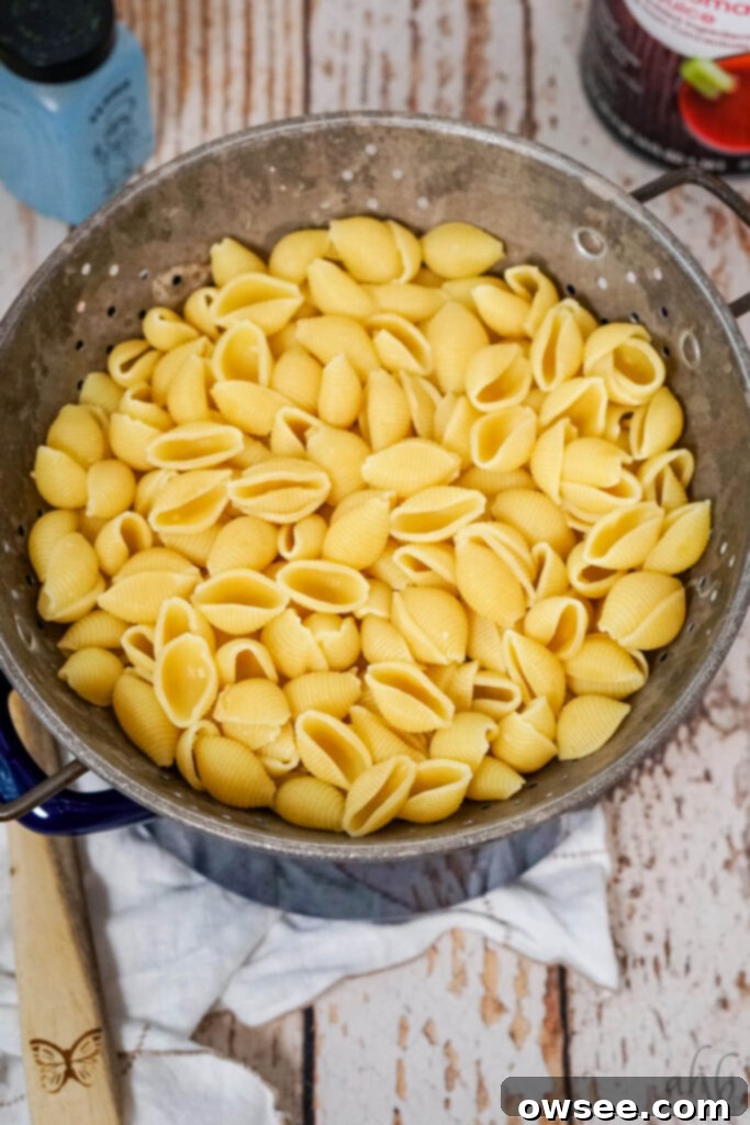 Homestyle Tomato Macaroni Comfort 6 Boiled and drained shell pasta rests in a colander on top of a blue stockpot, ready for the next step.