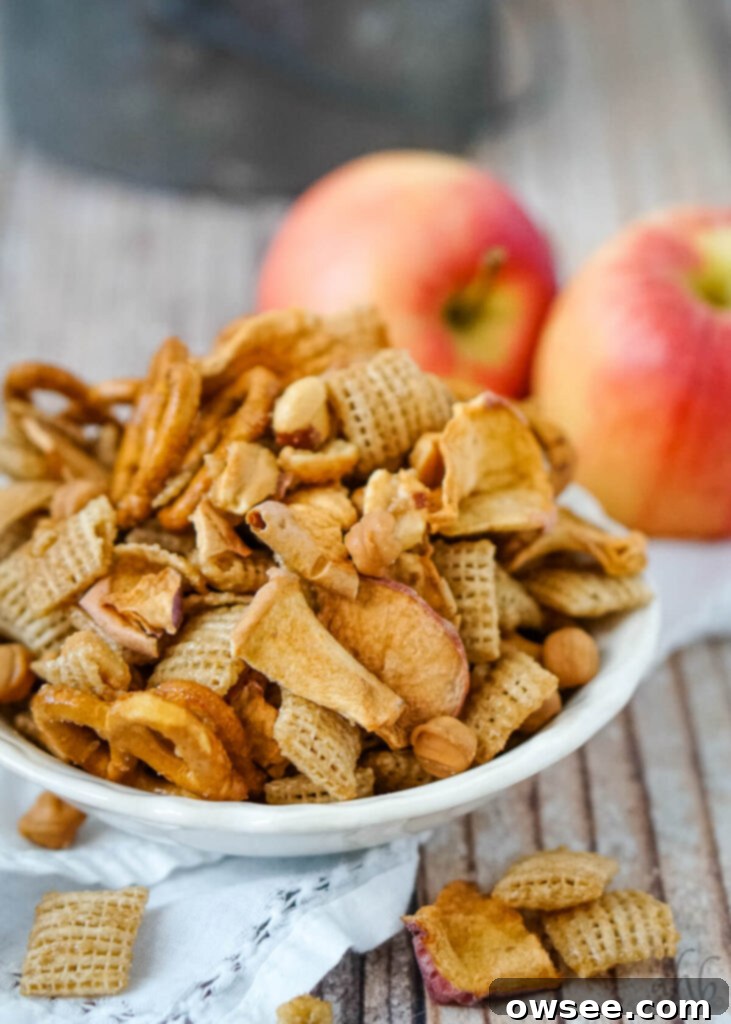 Golden Apple Caramel Crunch 3 A serving of Carmel Apple Chex Mix in a white dish in front of two apples.