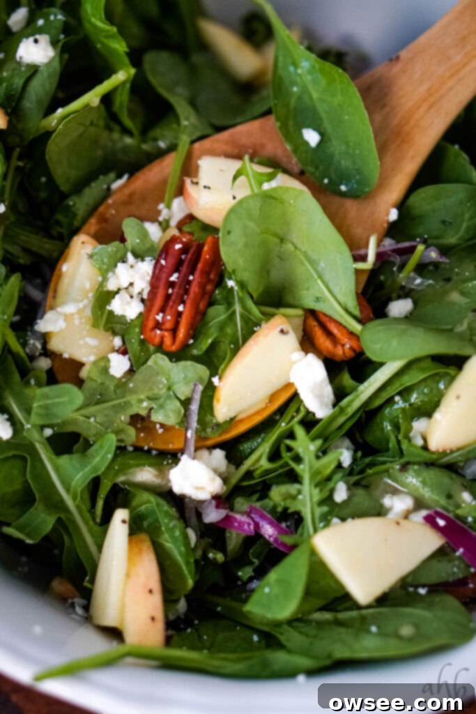 Crisp Apple, Creamy Feta and Spinach Salad 6 A wooden spoon lifting a spoonful of Apple Feta Spinach Salad, showing a toasted pecan, fresh spinach, apple slices, and feta cheese.