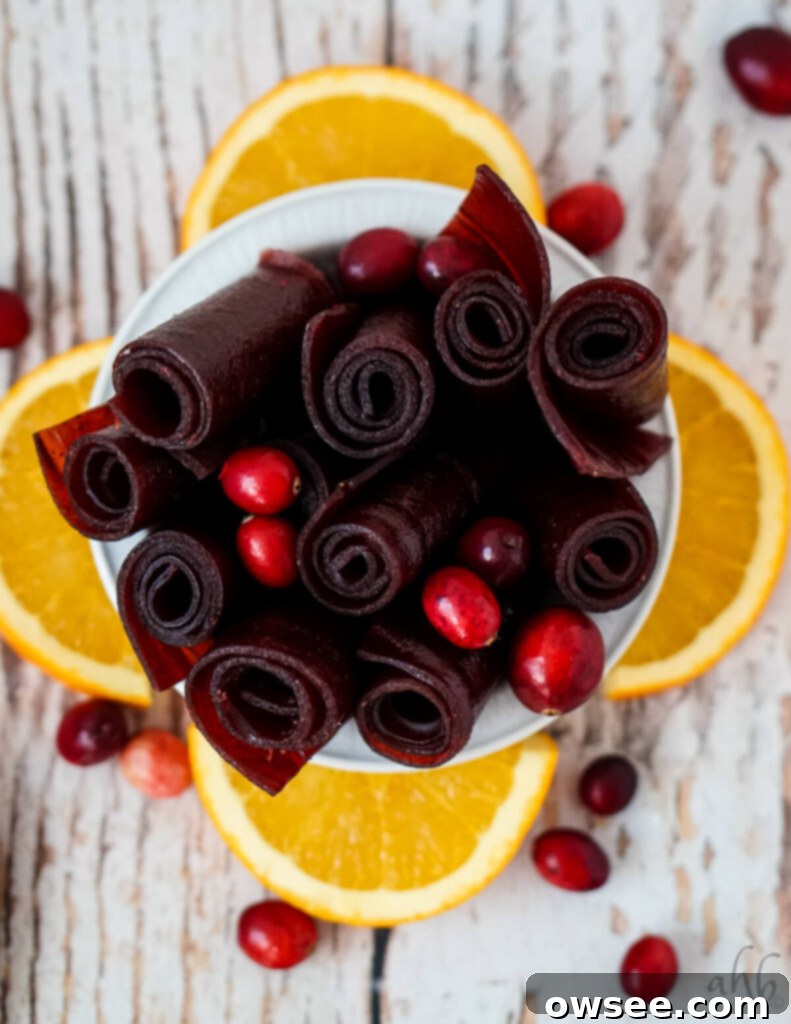Zesty Cranberry Orange Fruit Strips 3 A white bowl of cranberry fruit leather rolls with orange slices and cranberries.