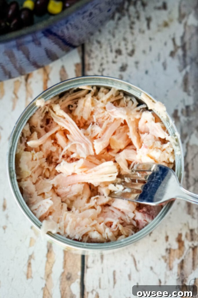 Effortless Seven Can Chicken Taco Soup 7 A can of chunked chicken breast with a fork shredding the chicken inside, demonstrating the preparation step.